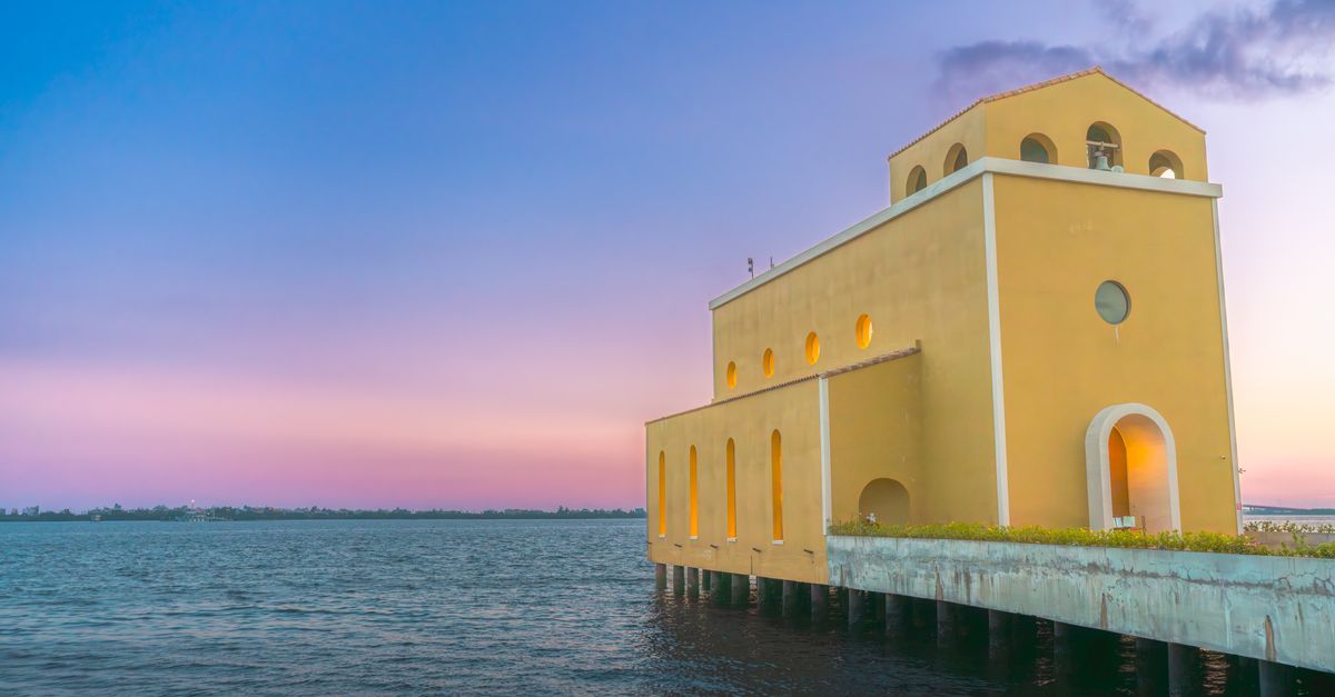 A picturesque yellow building on a pier at dusk, with a serene sea view under a colorful sky.